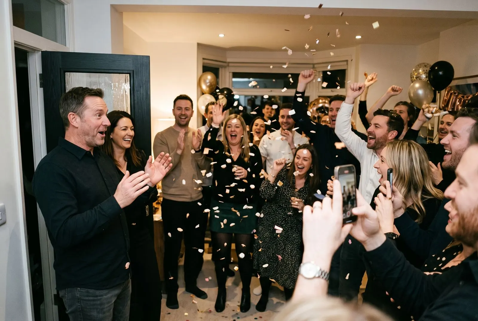 Friends cheer and throw confetti as the guest of honour walks into his surprise birthday party