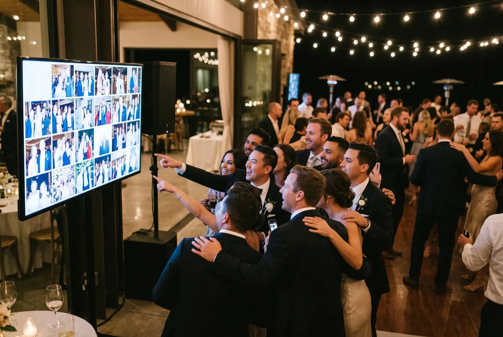 Wedding guests point at their photos on the live slideshow screen at the reception